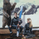 A snowboarding couple and a bear behind them