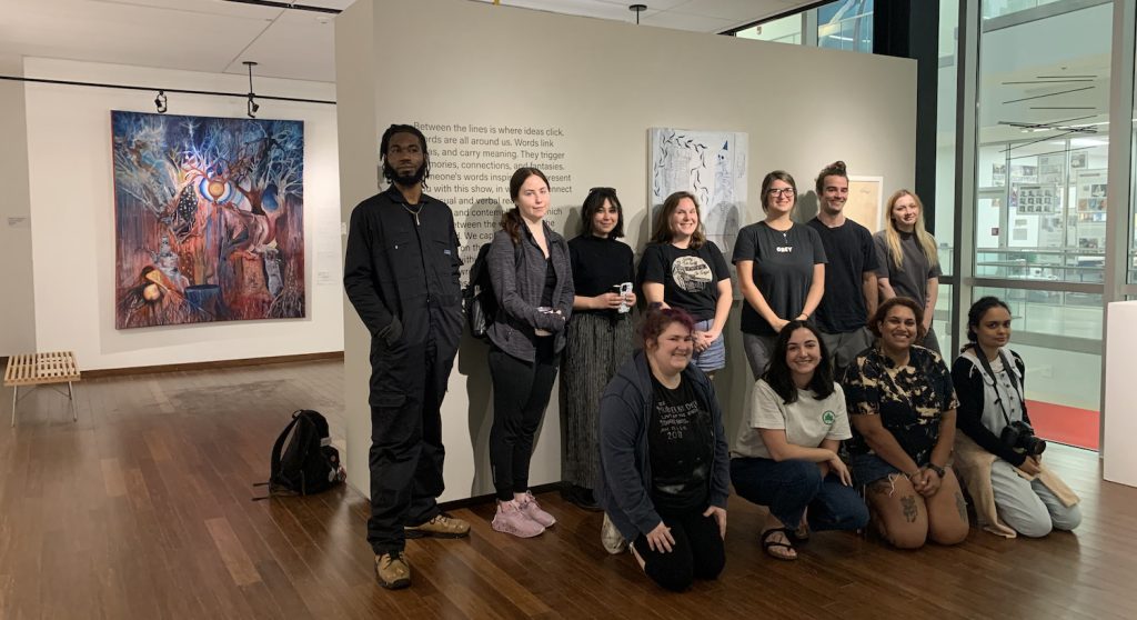 A group of students poses in front of well lit artwork in FSU's WJB gallery.