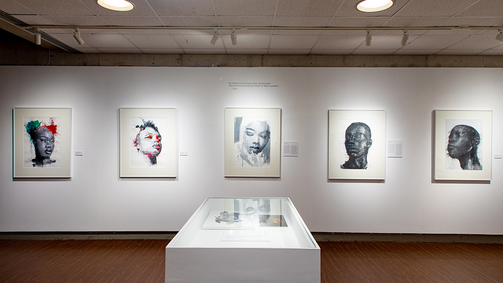 A series of modern portraits hang in a museum gallery.