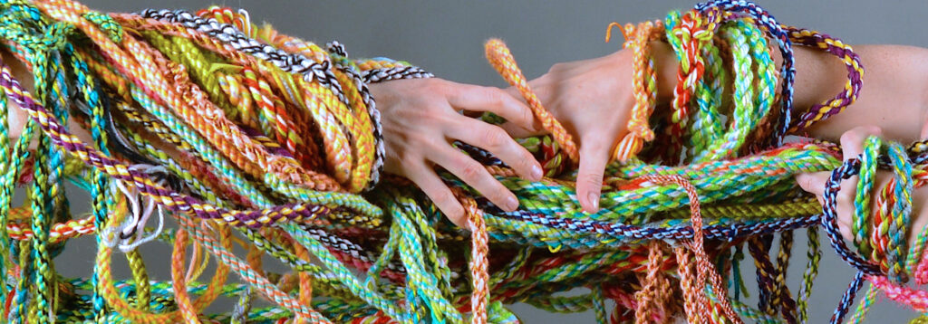 Hands reaching for each other, covered in colorful ropes.