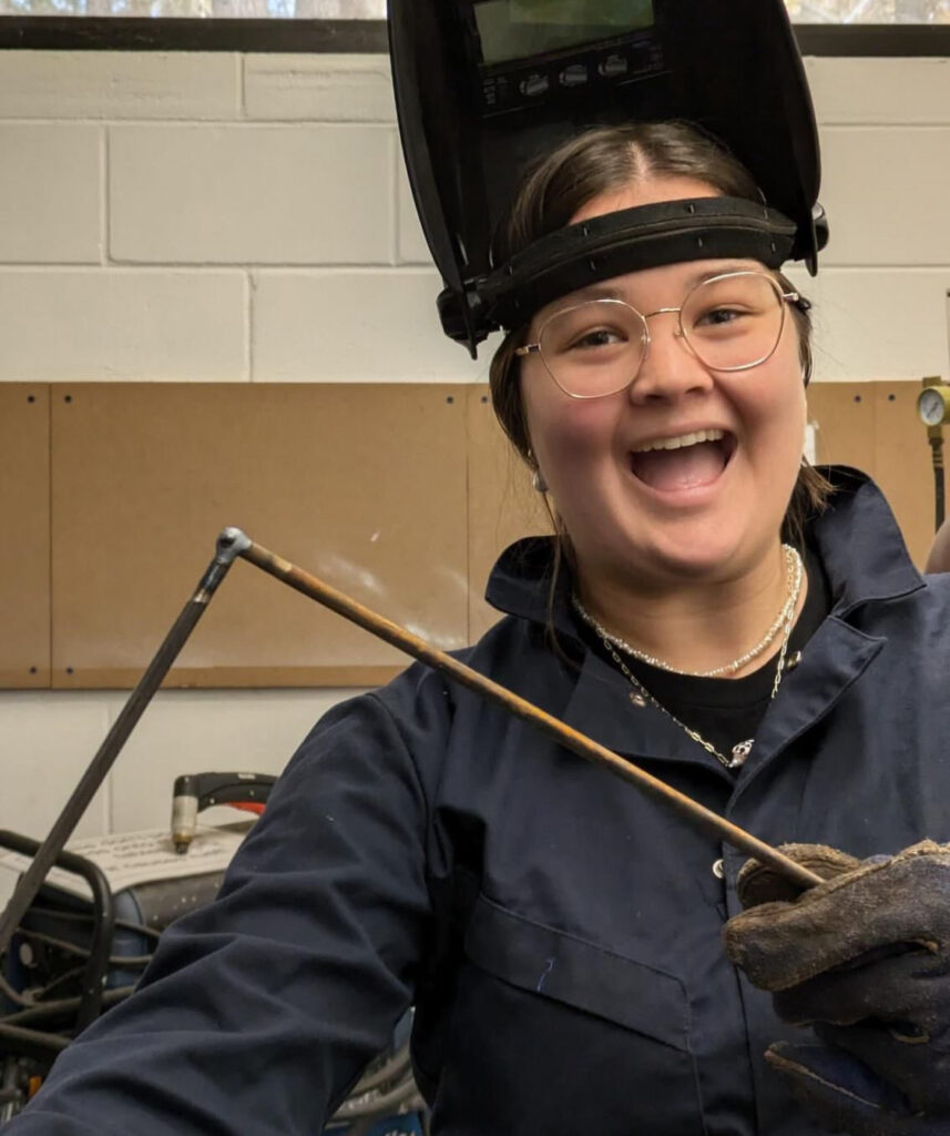 there is a woman that is wearing a welding helmet and holding a stick