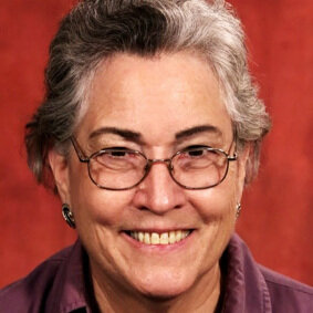 there is a woman with glasses smiling and wearing a purple shirt