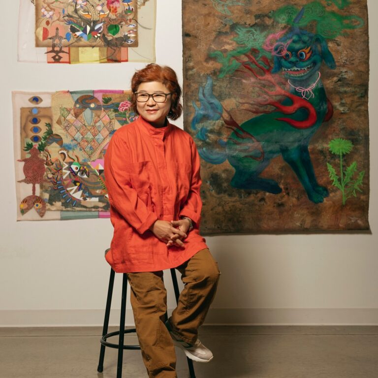 there is a woman that is sitting on a stool in front of a painting