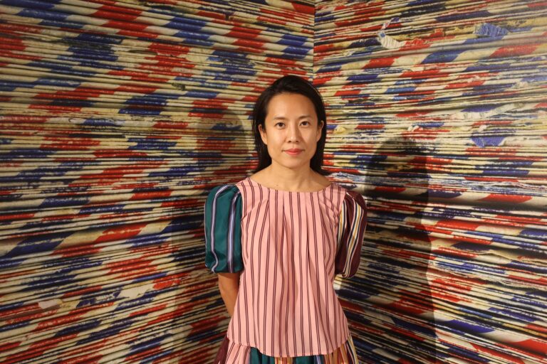 there is a woman standing in front of a wall covered with colorful papers