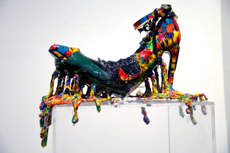 there is a sculpture of a woman sitting on top of a shoe covered in multicolored paint