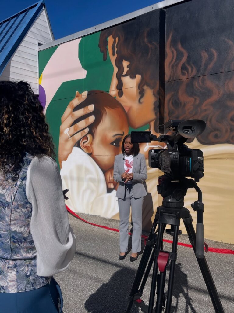 there is a woman standing in front of a painting with a camera on a tripod
