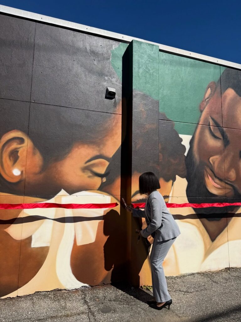 there is a woman standing in front of a wall with a painting on it