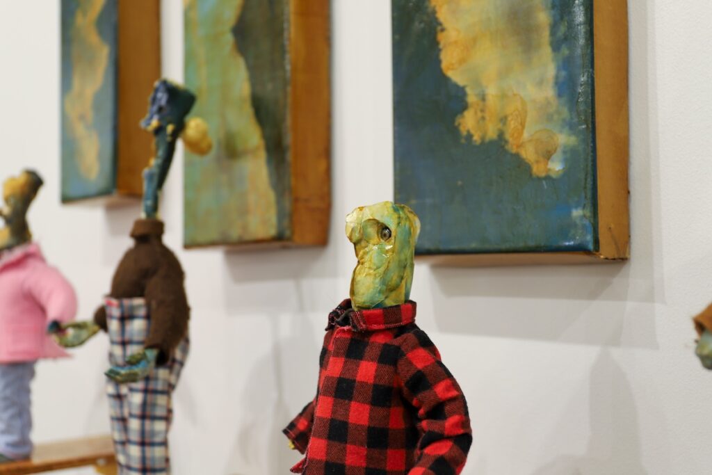 A closeup of a strange-looking doll with a green face and a plaid jacket. 