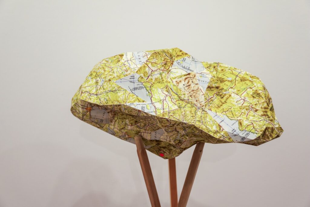 A sculpture made up of paper maps, made into an irregular shape, held up by wooden rods. 