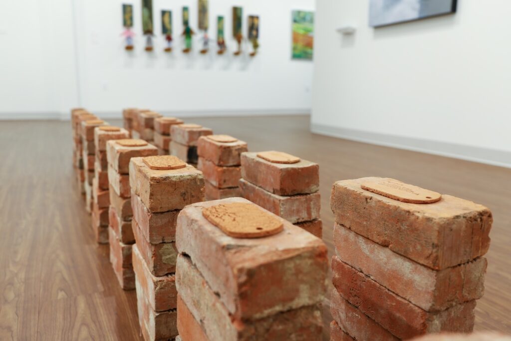 An art installation made up of bricks and clay molded dog tags on a vinyl floor. 