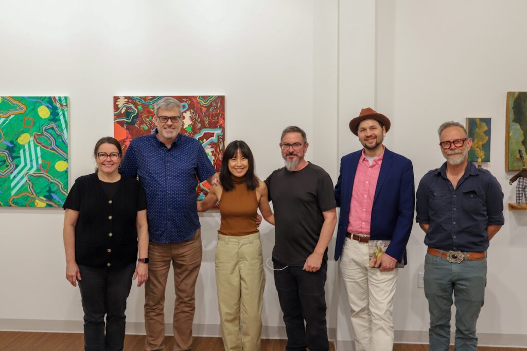 Six people pose for a group photo in an art gallery.